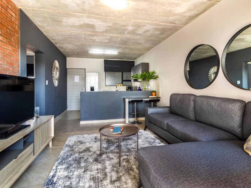 Modern open-plan living area featuring an exposed concrete ceiling, brick feature wall, and a functional kitchen with a breakfast bar.