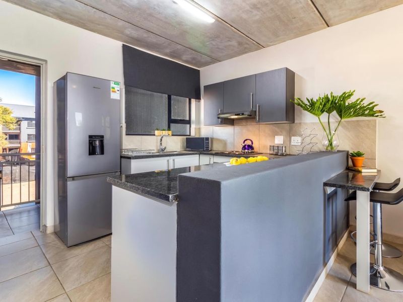 Modern kitchen featuring granite countertops, dark cabinetry, and an exposed concrete ceiling, with direct access to an outdoor balcony area.