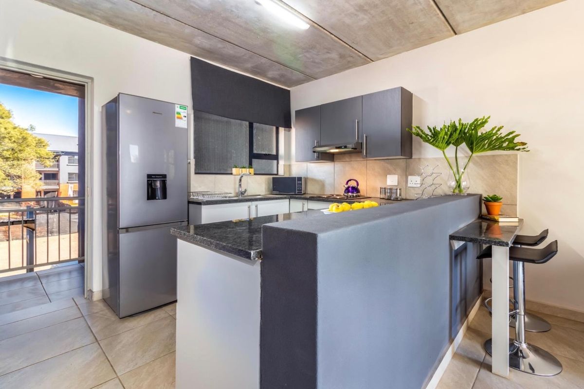Modern kitchen featuring granite countertops, dark cabinetry, and an exposed concrete ceiling, with direct access to an outdoor balcony area.