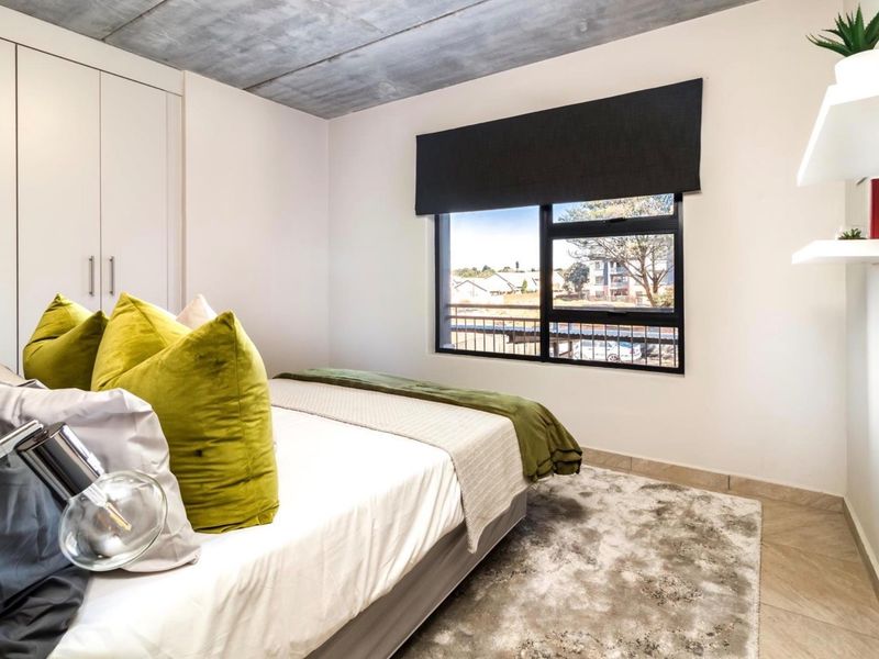Modern bedroom featuring an exposed concrete ceiling, built-in cupboards, tiled flooring, and a large window with a black frame providing natural light.