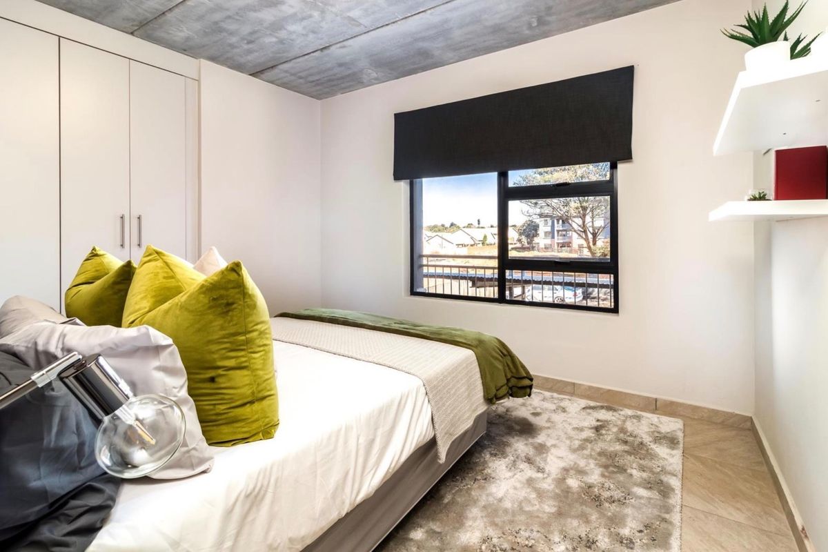Modern bedroom featuring an exposed concrete ceiling, built-in cupboards, tiled flooring, and a large window with a black frame providing natural light.