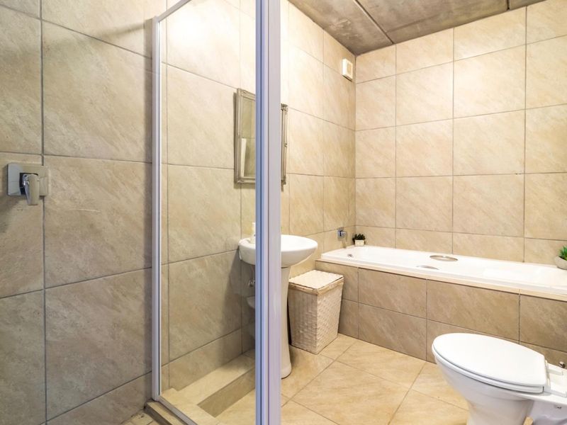 A functional bathroom featuring a pedestal basin, a separate shower enclosure, a built-in bathtub, and a toilet, finished with neutral wall and floor tiles.