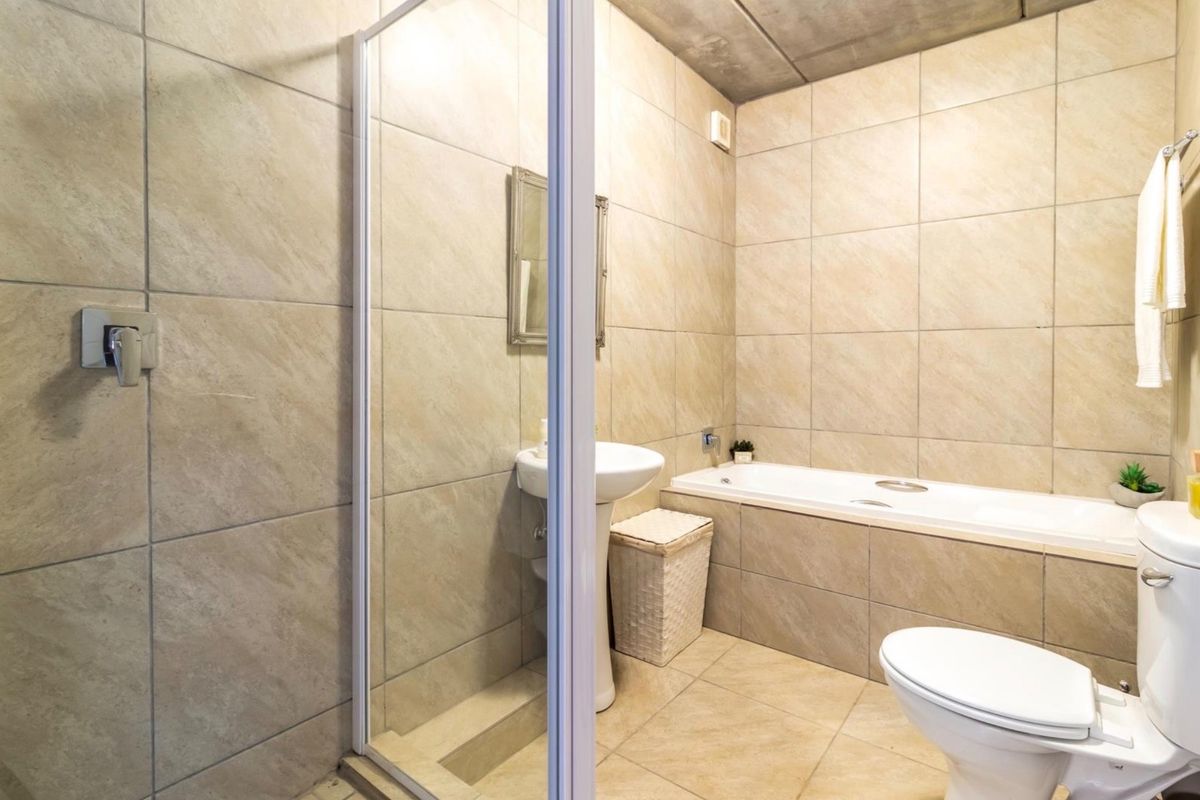 A functional bathroom featuring a pedestal basin, a separate shower enclosure, a built-in bathtub, and a toilet, finished with neutral wall and floor tiles.