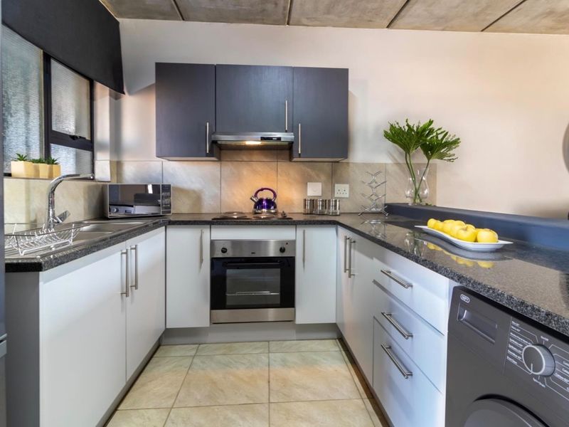 Modern U-shaped kitchen featuring dark and light cabinetry, granite countertops, integrated oven and hob, and a contemporary exposed concrete ceiling finish.