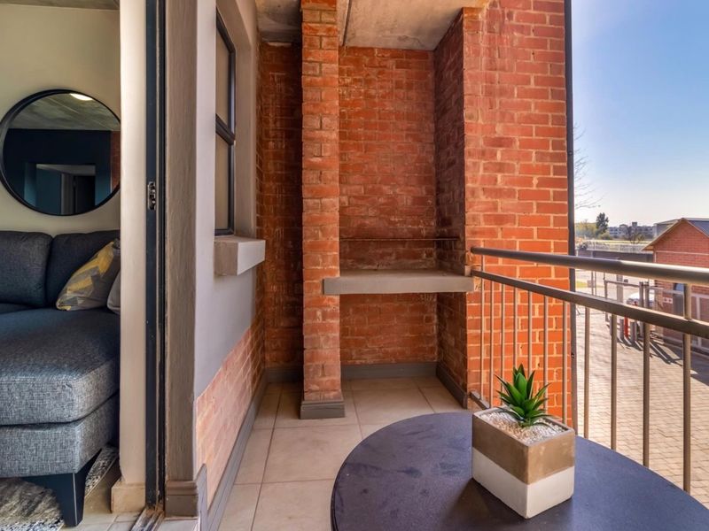 A private balcony featuring a built-in brick braai, tiled flooring, and metal safety railings, offering an outdoor space for relaxation.