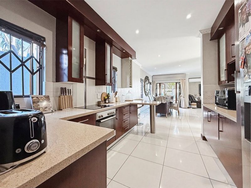 Spacious open-plan kitchen featuring dark wood cabinetry, stone countertops, and integrated appliances, flowing seamlessly into the adjacent dining and living areas.