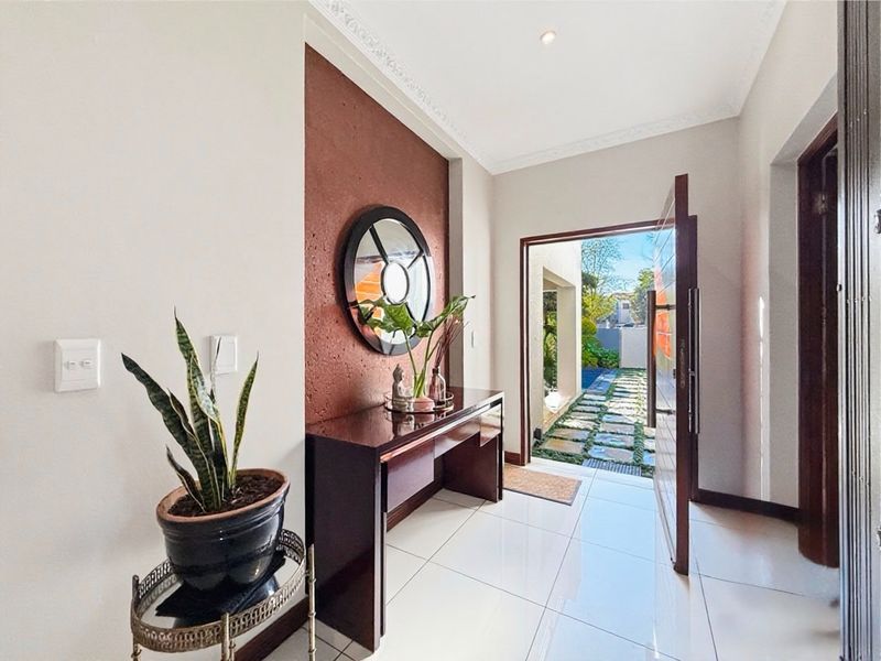 Bright entrance foyer featuring polished floor tiles, a textured feature wall, and decorative cornice, leading directly to an outdoor garden pathway.