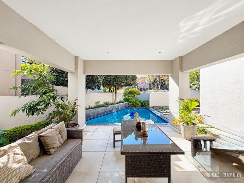 A covered patio area featuring tiled flooring and recessed lighting, overlooking a private swimming pool and landscaped garden.