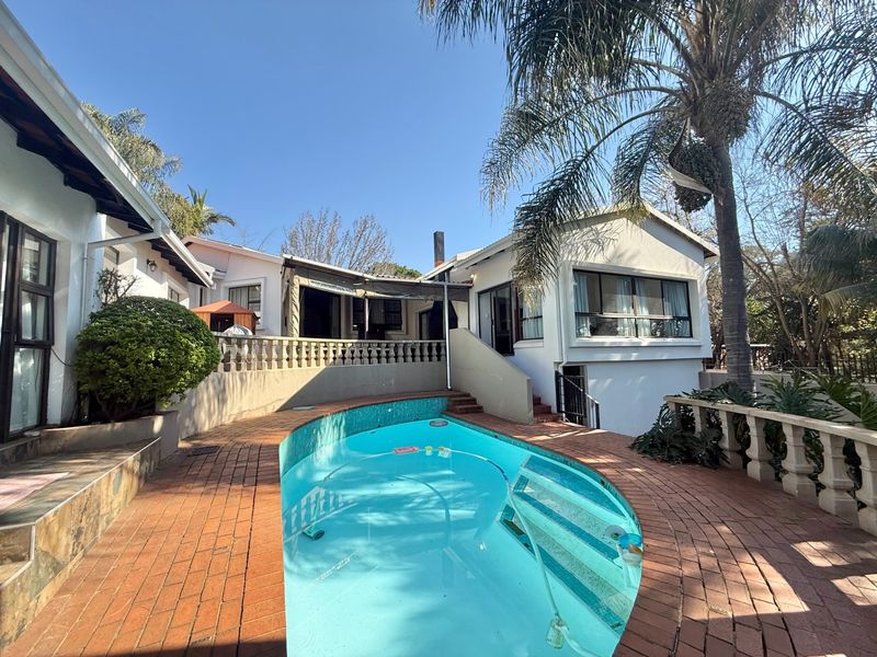 Rear exterior view featuring a swimming pool, brick paved surround, and a raised patio area with balustrades, set against the house facade.