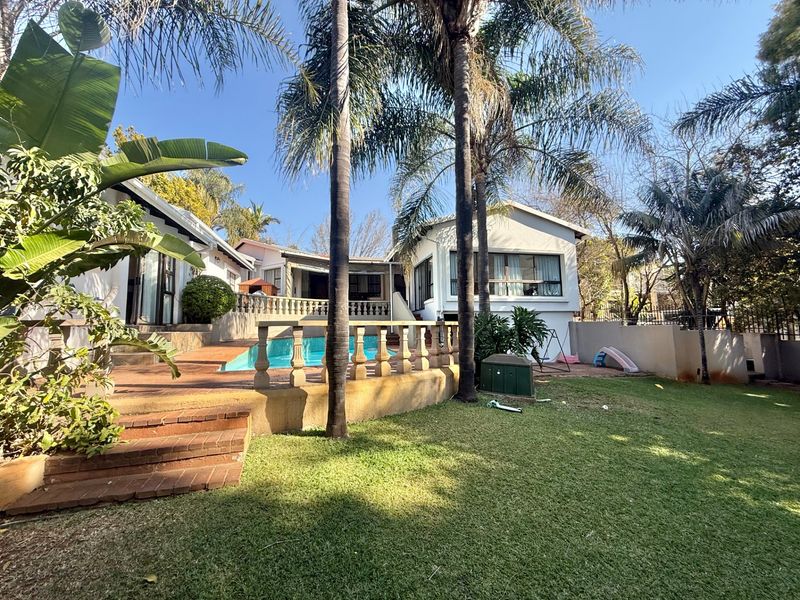 Rear exterior view featuring a swimming pool, brick patio area, and established garden with mature palm trees.