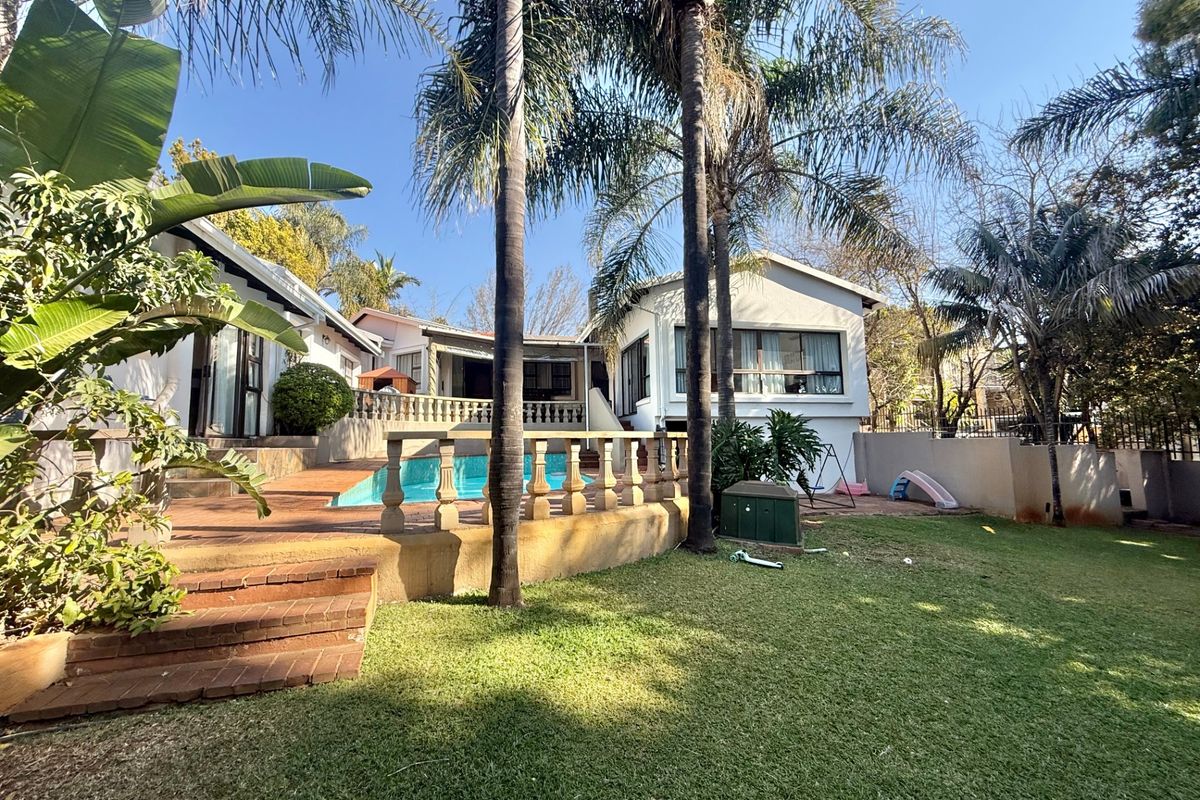 Rear exterior view featuring a swimming pool, brick patio area, and established garden with mature palm trees.