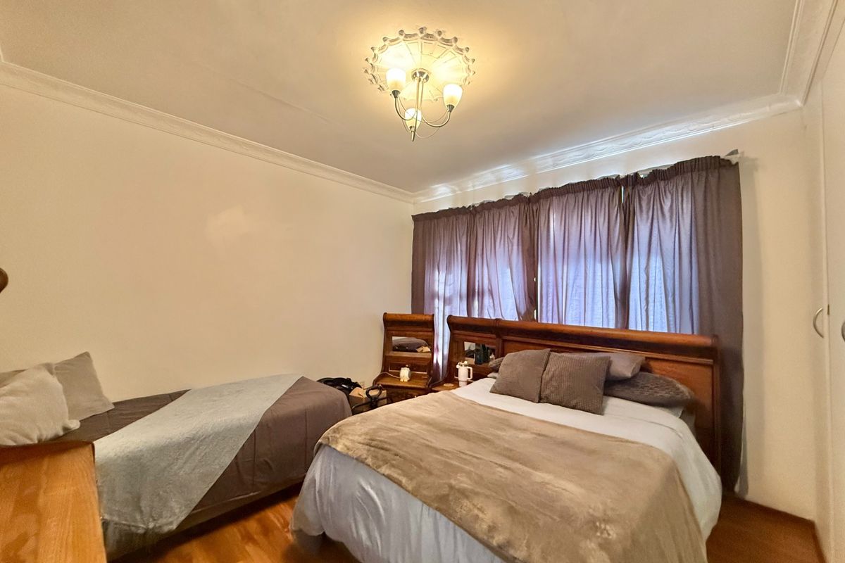 A bedroom featuring hardwood flooring, crown molding, and a central ceiling light fixture.