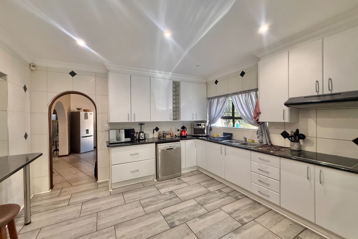 A functional kitchen featuring white cabinetry, dark granite countertops, tiled flooring, and a distinctive arched doorway leading to adjacent living spaces.