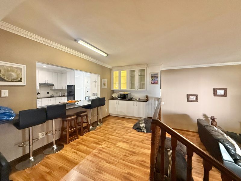 Open plan living area featuring laminate flooring, a breakfast bar, and built-in cabinetry with glass-fronted display units, overlooking a staircase.