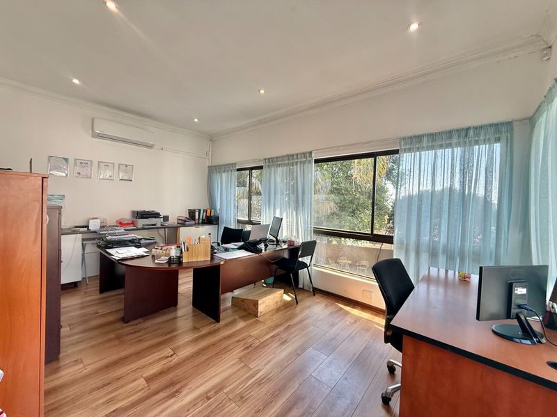 A bright and functional home office featuring laminate flooring, recessed lighting, a split-system air conditioner, and large windows providing ample natural light.