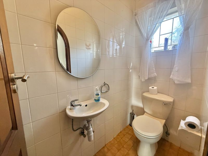 A compact guest bathroom featuring a wall-mounted basin, close-coupled toilet, and full-height ceramic wall tiling.