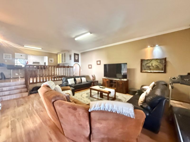 Spacious open-plan living area featuring timber flooring, a raised kitchen platform with wooden balustrade, and coved cornicing throughout.