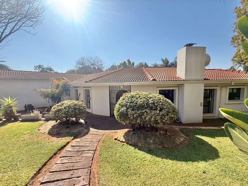 A rear view of the house featuring a terracotta tiled roof, masonry chimney, and a brick-paved pathway leading through the garden.