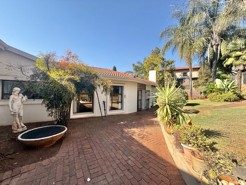 A well-maintained rear exterior view featuring a brick-paved patio area, landscaped garden, and a classic tiled roof structure.