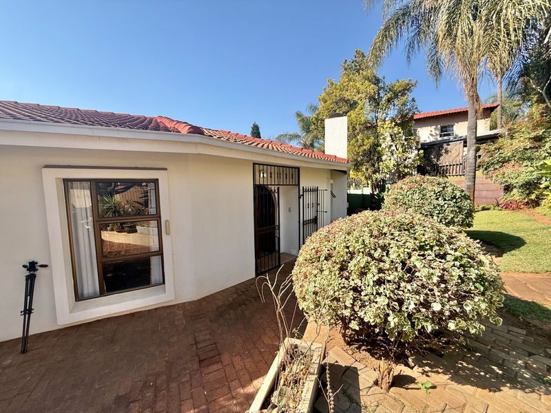 Rear exterior view of the house featuring a brick paved patio, terracotta roof tiles, and a secure metal entrance gate.