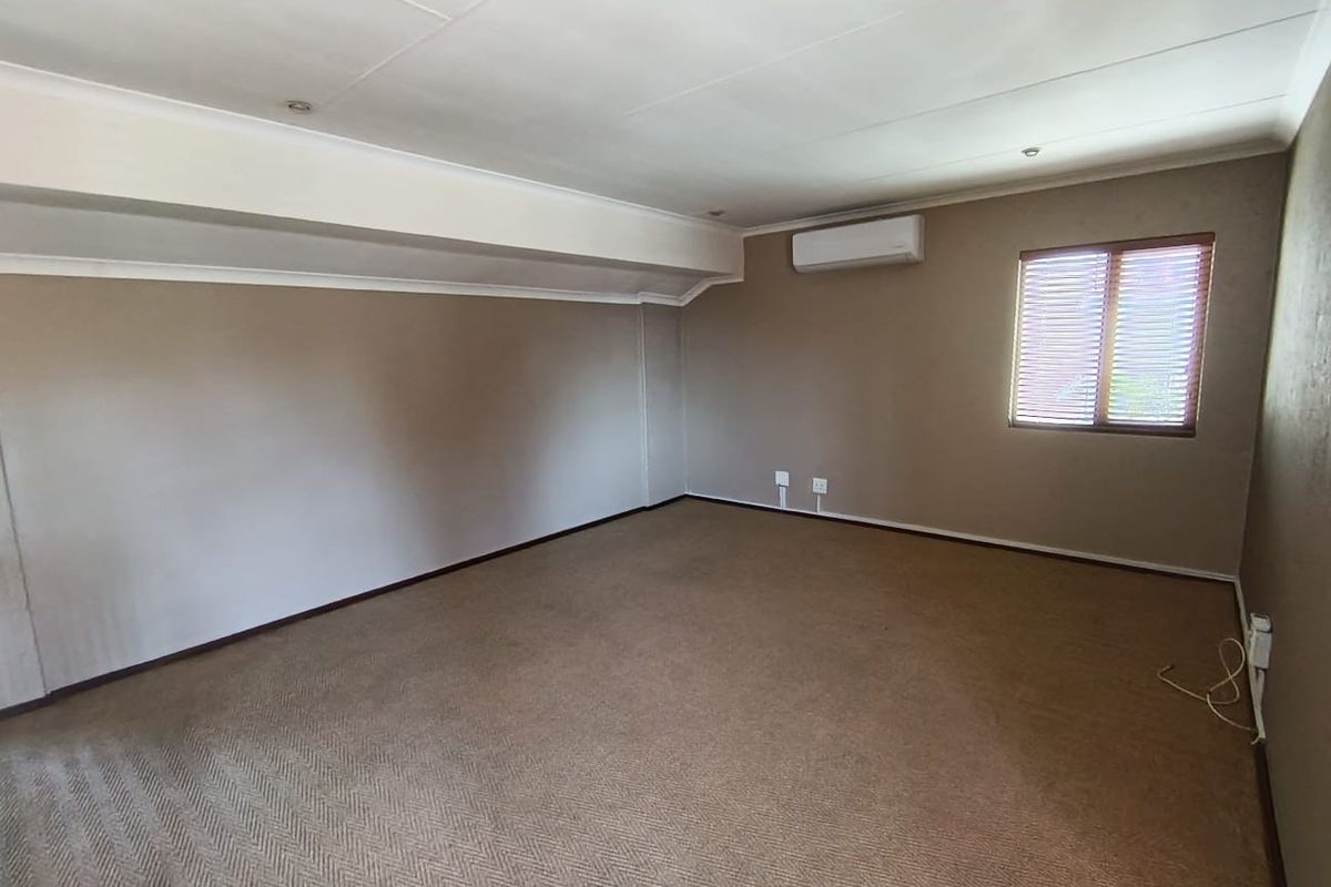 A spacious, empty bedroom featuring neutral wall tones, carpeted flooring, an integrated air conditioning unit, and recessed ceiling lighting.