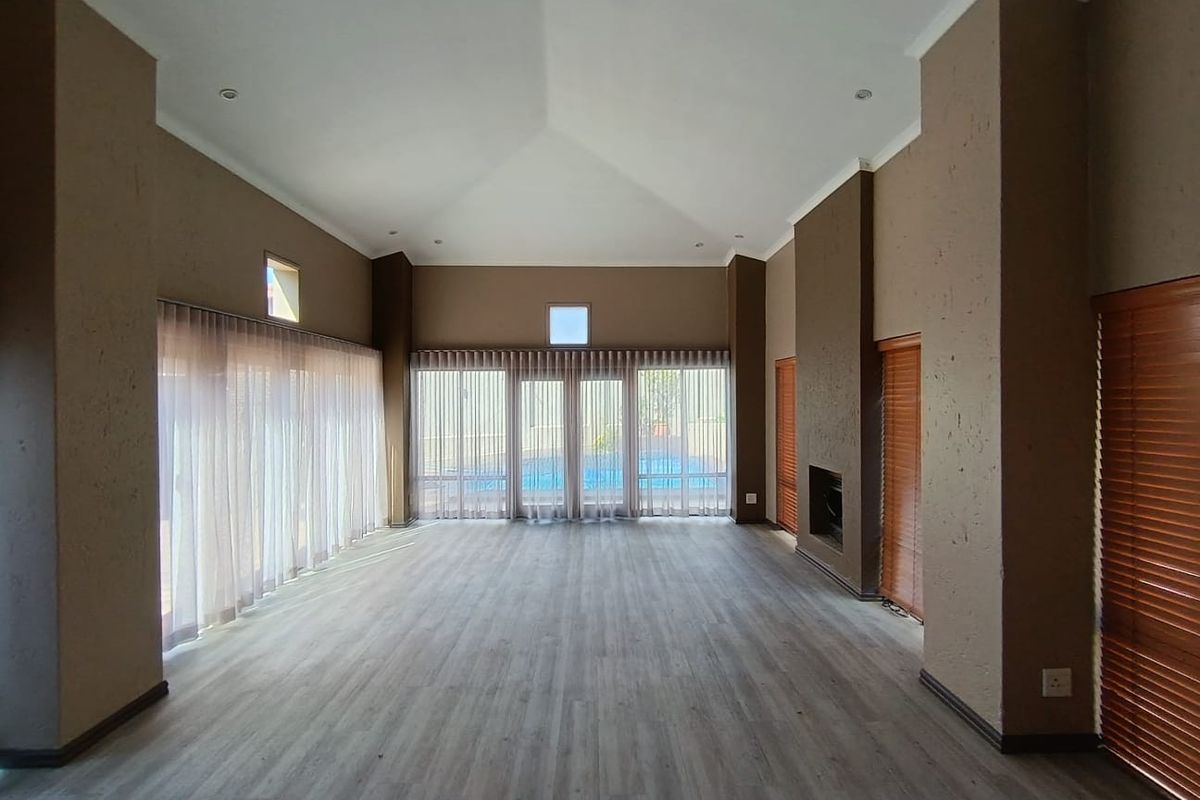 Spacious living room featuring a high vaulted ceiling, modern laminate flooring, and a built-in fireplace with direct access to the pool area.