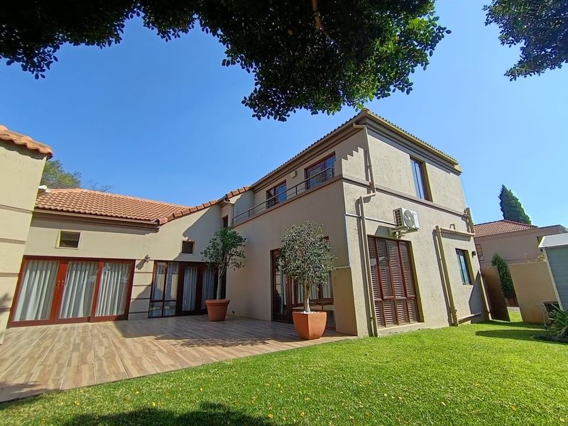 Rear view of the house featuring a spacious tiled patio, well-maintained lawn, and upper-level balcony access with integrated air conditioning.