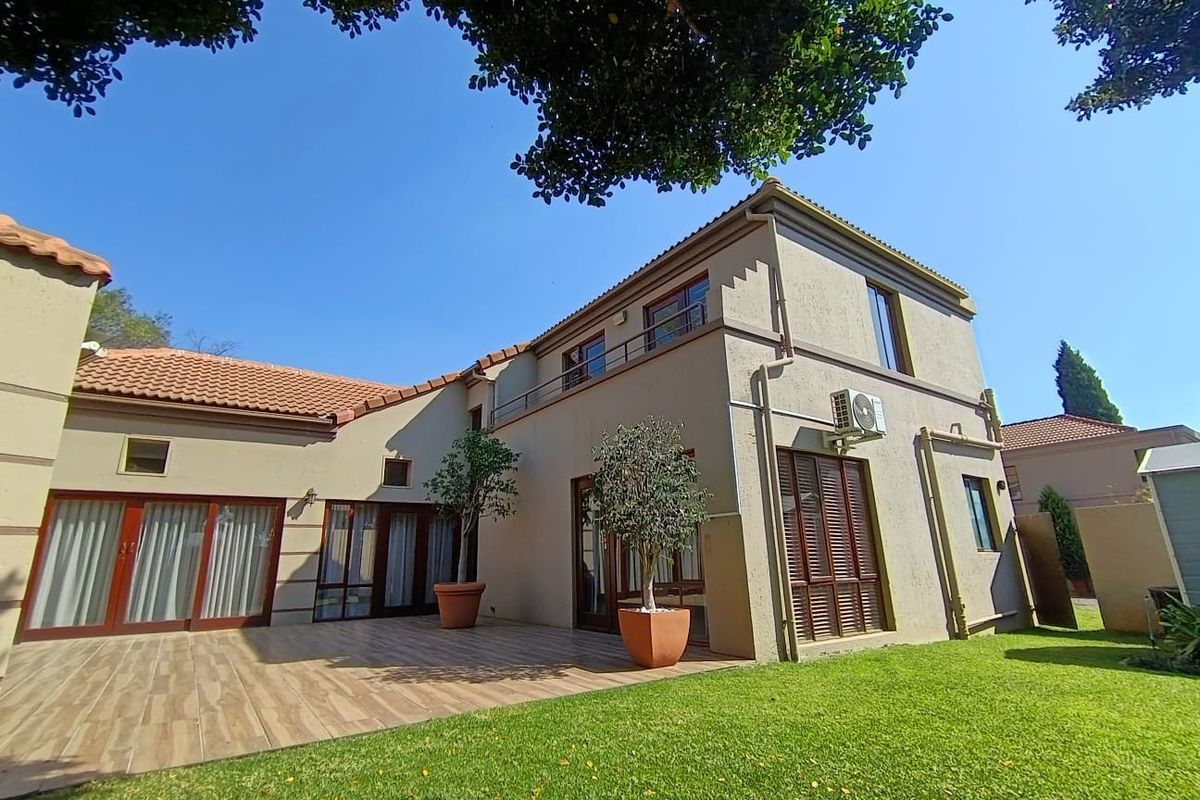 Rear view of the house featuring a spacious tiled patio, well-maintained lawn, and upper-level balcony access with integrated air conditioning.
