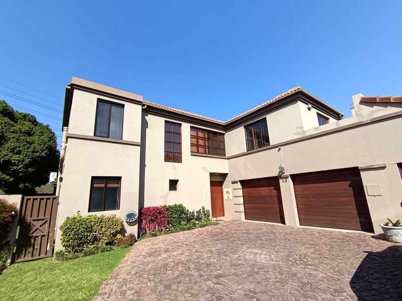 Front elevation of a double-storey residence featuring a paved driveway, double garage with timber doors, and a well-maintained exterior facade.