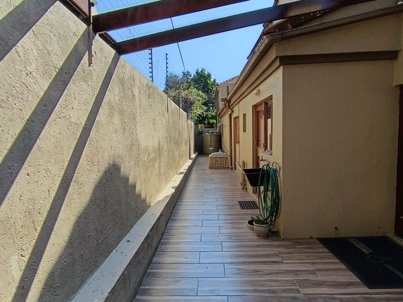 A side patio area featuring wood-look tiled flooring, a timber pergola structure, and a secure boundary wall with electric fencing.