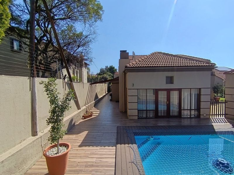 A well-maintained outdoor pool area featuring a tiled patio, secure boundary wall with electric fencing, and direct access to the home via french doors.