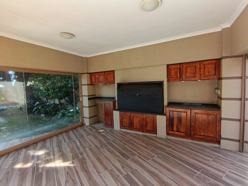 Covered patio area featuring a built-in braai, wooden cabinetry with stone countertops, and large sliding glass doors overlooking the garden.
