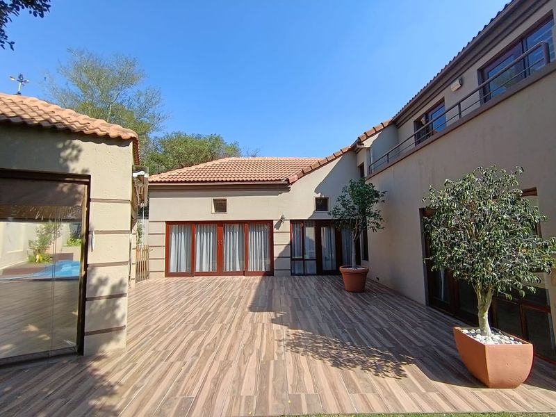 A spacious rear patio area featuring wood-look tiling, terracotta roof tiles, and multiple glass sliding doors providing access to the home's interior.