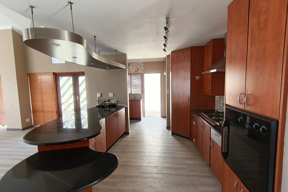 Spacious kitchen featuring wood-finish cabinetry, granite countertops, a breakfast bar, and built-in appliances, offering a functional layout with direct access to the exterior.