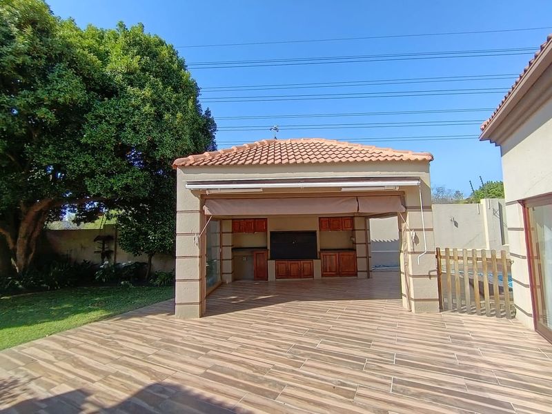 Spacious covered outdoor patio featuring built-in cabinetry, a built-in braai, and a retractable awning, perfect for alfresco dining and entertaining.