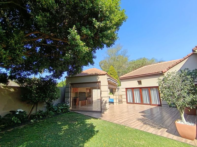A well-maintained rear garden featuring a tiled patio, a covered outdoor entertainment area, and established landscaping under a clear blue sky.