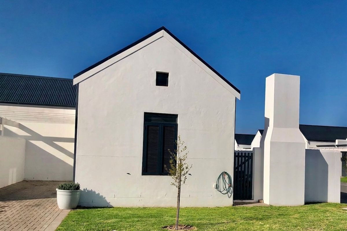 A well-maintained rear exterior view of the property featuring a clean white facade, dark metal roof, external chimney, and a neat lawn area.