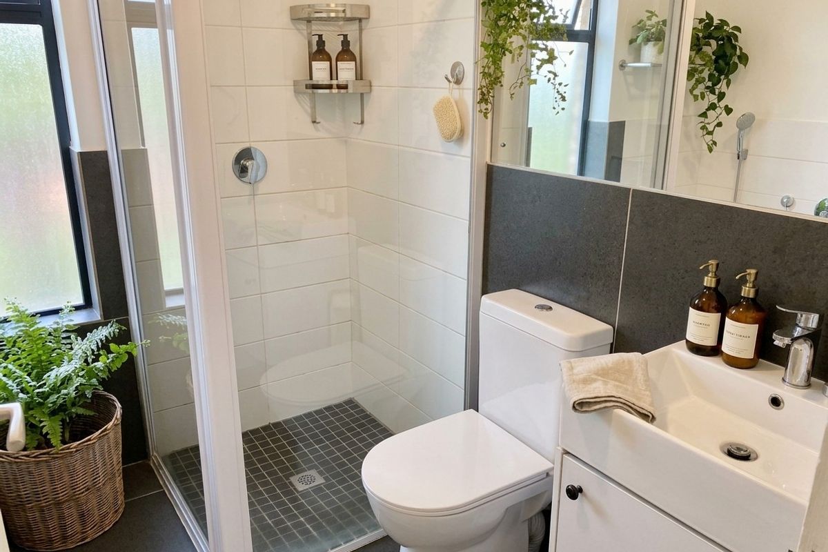 A modern, compact bathroom featuring a glass-enclosed shower, a sleek vanity basin, and contemporary dark and white wall tiling.