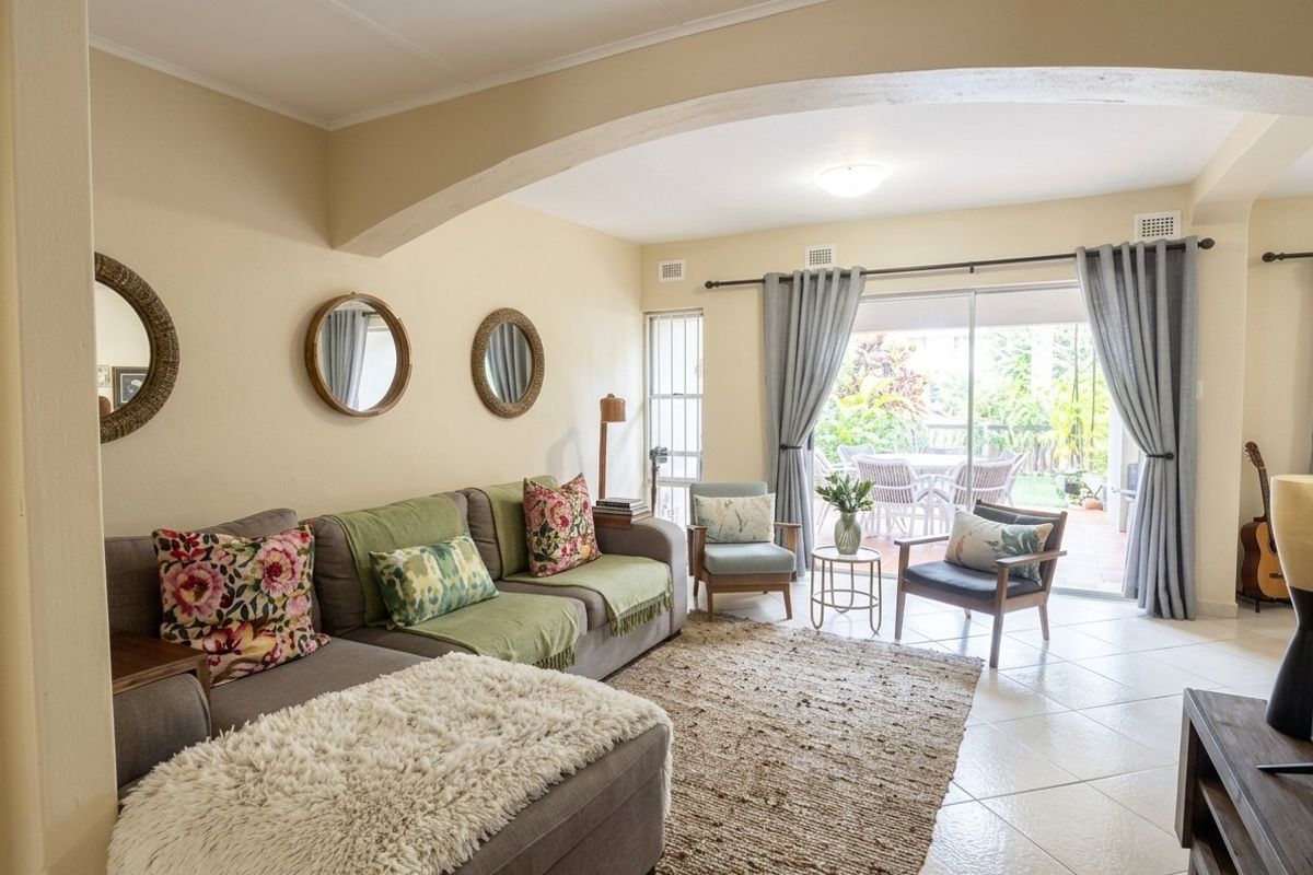 A bright and spacious living room featuring tiled flooring, an architectural archway, and large sliding glass doors providing direct access to the outdoor patio area.