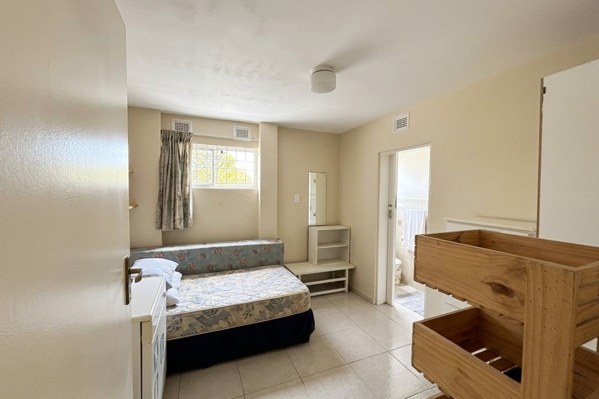 A bedroom featuring tiled flooring, security bars on the window, and direct access to an adjoining bathroom.