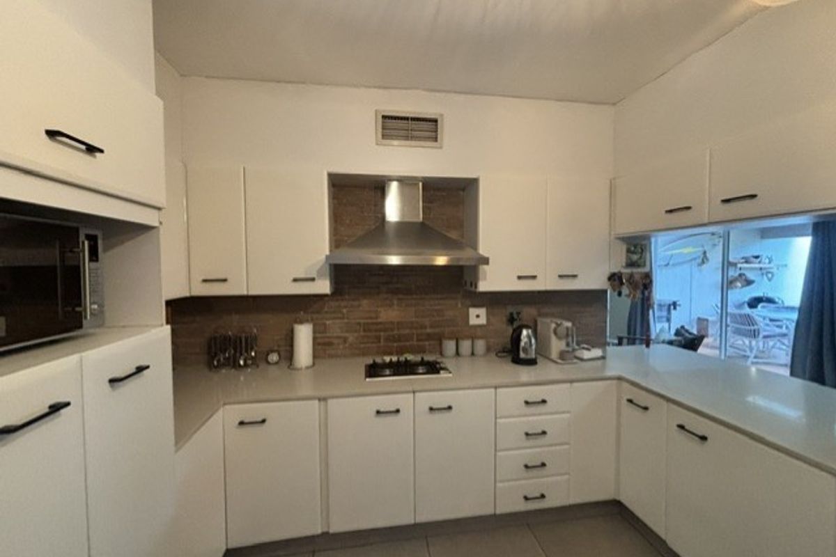 A functional kitchen featuring white cabinetry, stone countertops, a gas hob with extractor fan, and a brick-style backsplash, with direct access to an outdoor area.