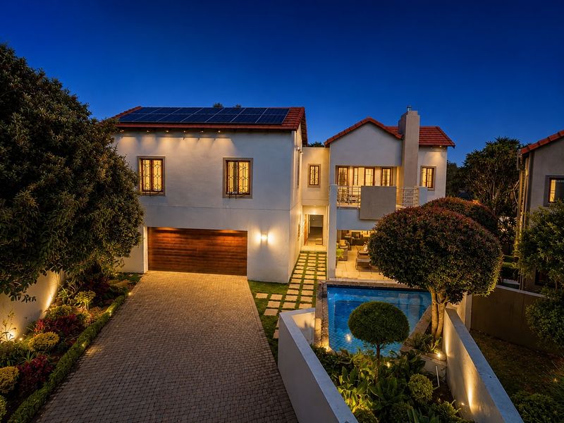 A well-maintained two-story house at dusk, featuring a paved driveway, double garage, swimming pool, and rooftop solar panels.