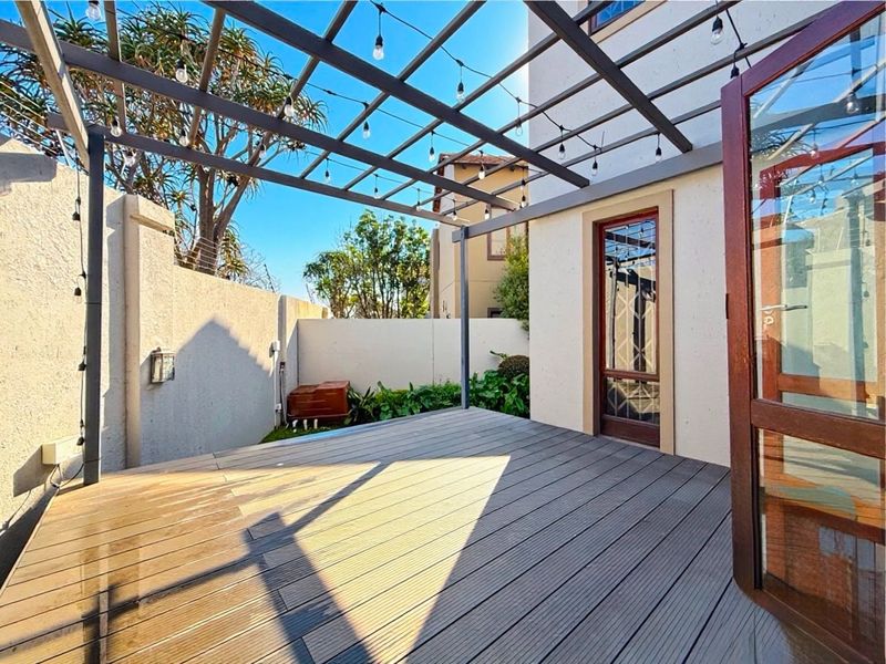 A well-maintained outdoor patio featuring timber decking and a modern pergola with integrated string lighting, providing a perfect space for outdoor entertaining.