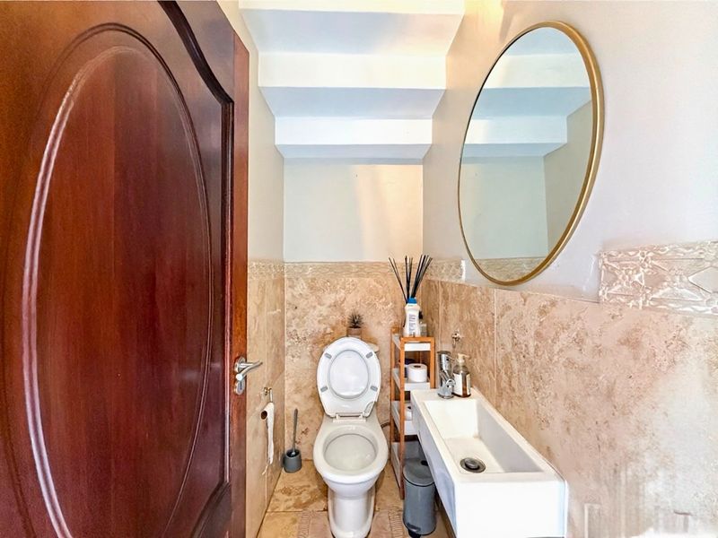 A compact guest bathroom featuring travertine wall and floor tiling, a wall-mounted basin with a mixer tap, and a solid wood door.