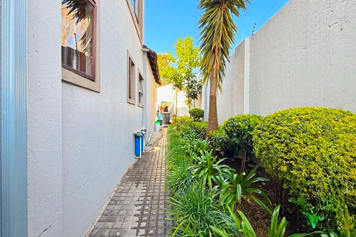 A side garden pathway featuring paved flooring, established landscaping, and a boundary wall, providing access along the side of the property.
