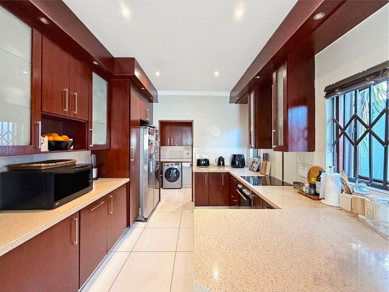 A well-maintained kitchen featuring dark wood cabinetry, stone countertops, recessed lighting, and a functional layout with an adjacent laundry area.