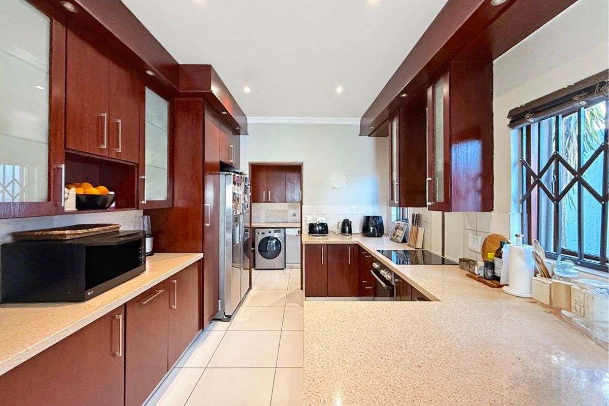 A well-maintained kitchen featuring dark wood cabinetry, stone countertops, recessed lighting, and a functional layout with an adjacent laundry area.