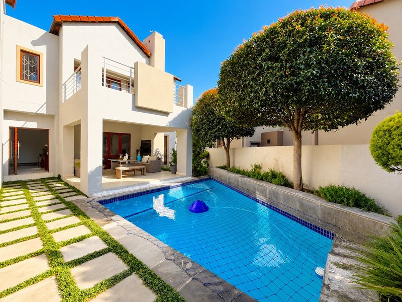 A well-maintained outdoor area featuring a swimming pool with a safety net, a covered patio, and a stone-paved walkway leading to the residence.