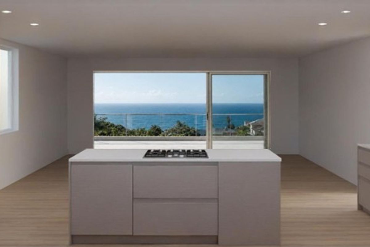 Modern open-plan kitchen featuring a central island with gas cooktop, integrated appliances, and expansive sliding doors opening to a scenic ocean view.