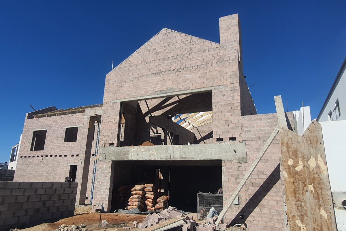 A rear view of a residential property currently under construction, featuring exposed concrete block walls and timber roof framing.